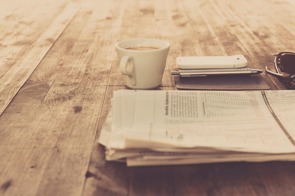 A warm vintage morning setup with coffee, newspaper, and smartphone on wooden table.